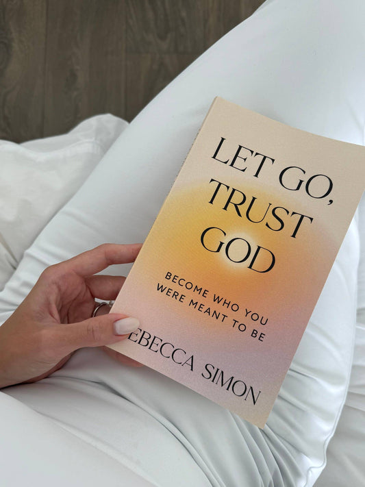 Book titled 'Let Go, Trust God' by Rebecca Simon held by a person on a white surface.