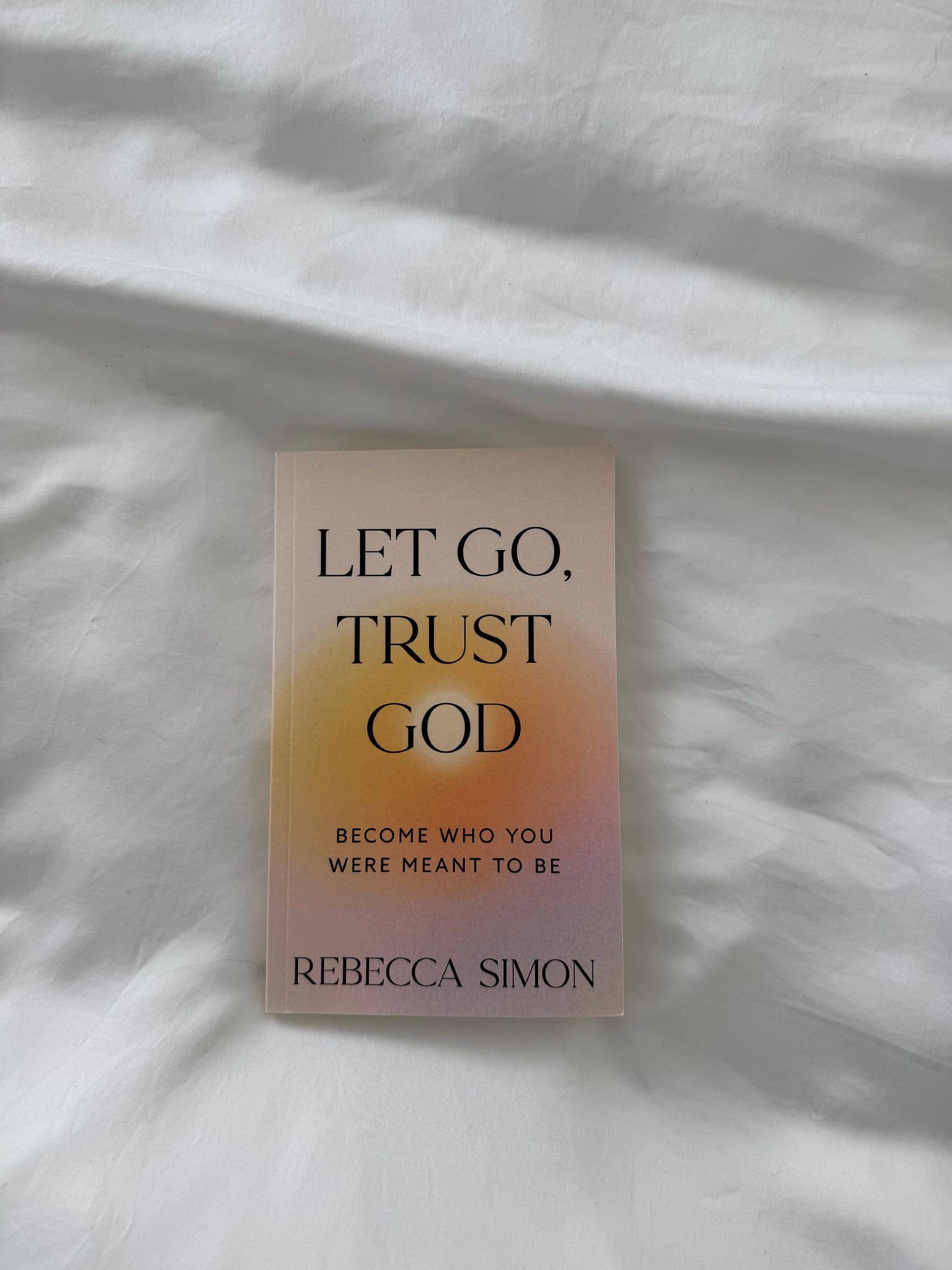 Book titled 'Let Go, Trust God' by Rebecca Simon on a textured white surface