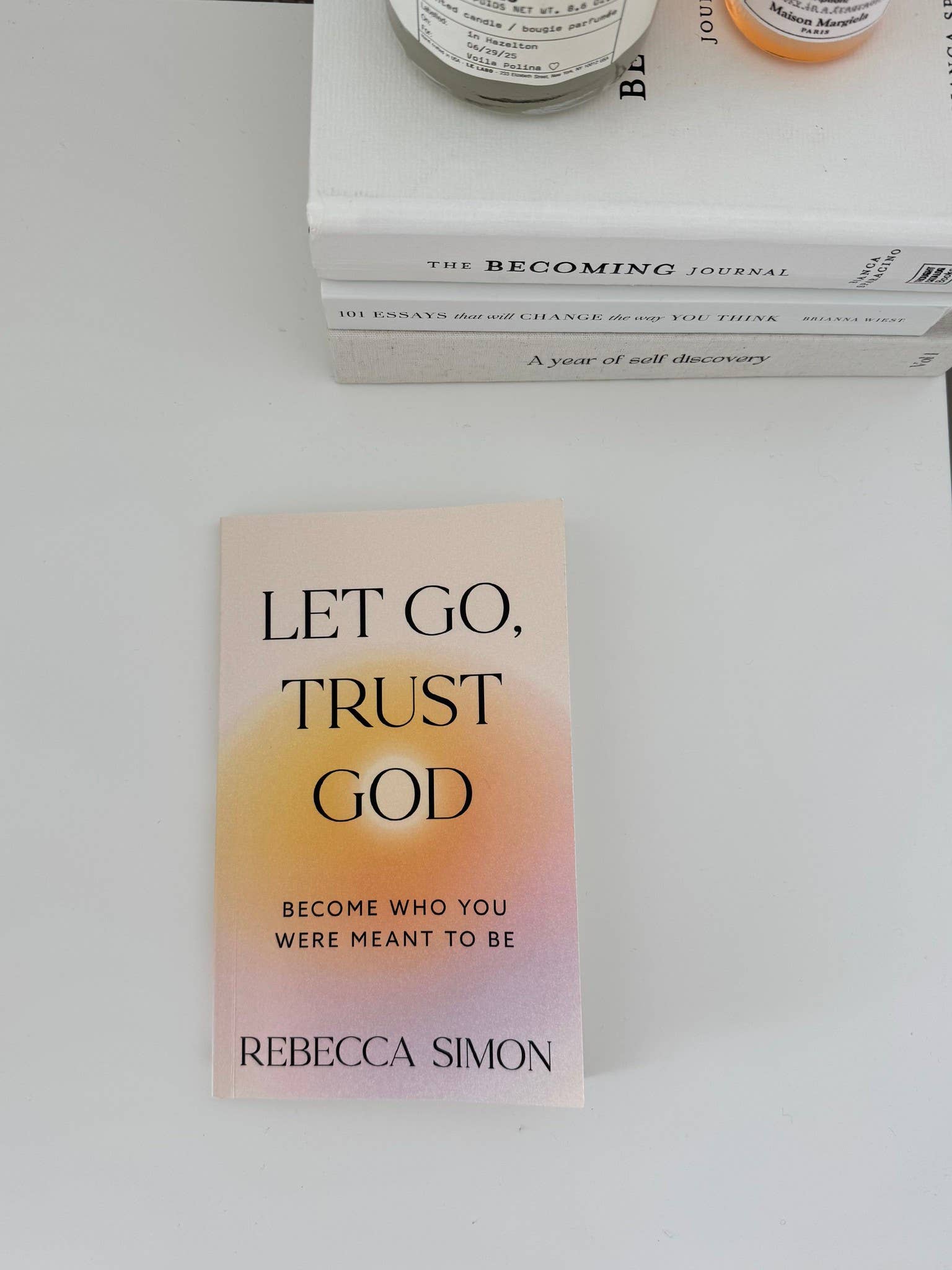 Book titled 'Let Go, Trust God' by Rebecca Simon on a white surface with a blurred background.