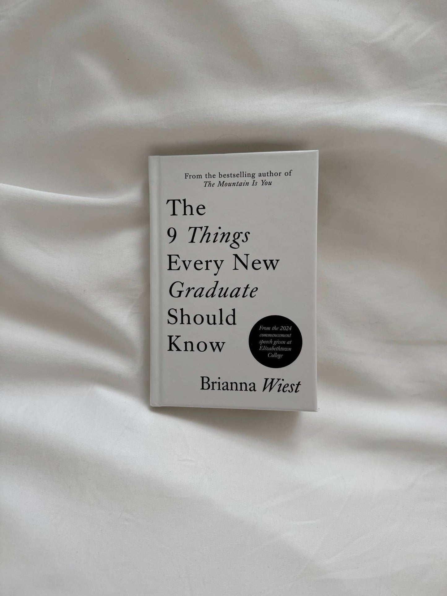 Book titled 'The 9 Things Every New Graduate Should Know' by Brianna Wiest on a white fabric background