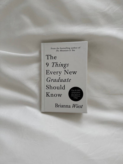 Book titled 'The 9 Things Every New Graduate Should Know' by Brianna Wiest on a white fabric background