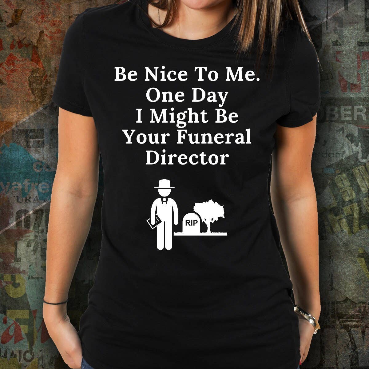 Person wearing a black t-shirt with humorous text and graphic design against a textured wall background.