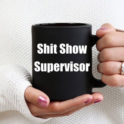 Black mug with 'Shit Show Supervisor' text held by a person against a white background