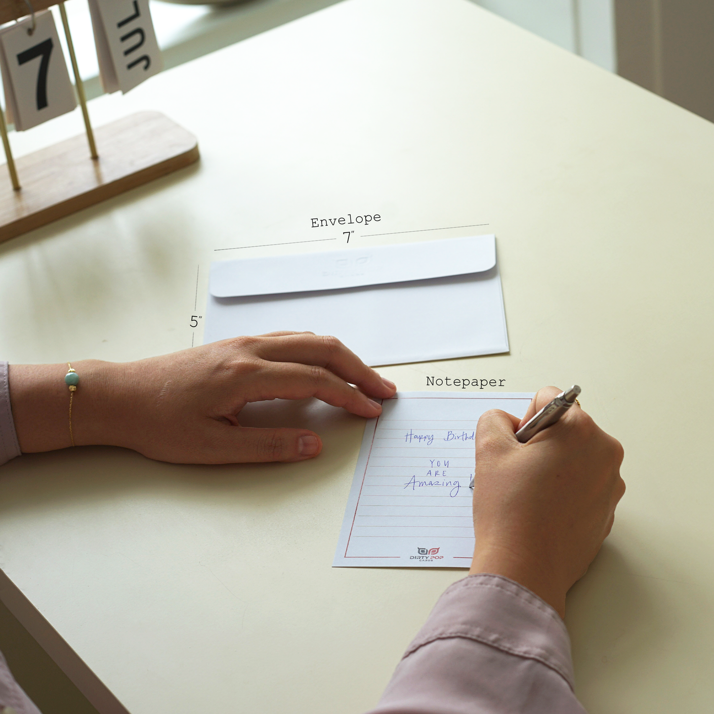 Person writing on a notepad with an envelope and stationery items on a table.
