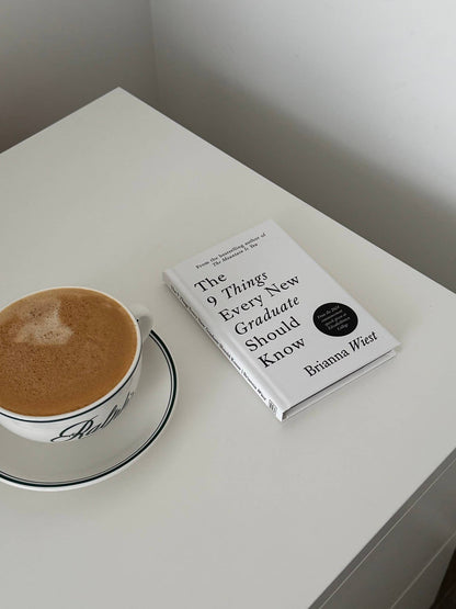 Book titled 'The 9 Things Every New Graduate Should Know' on a white surface with a cup of coffee.